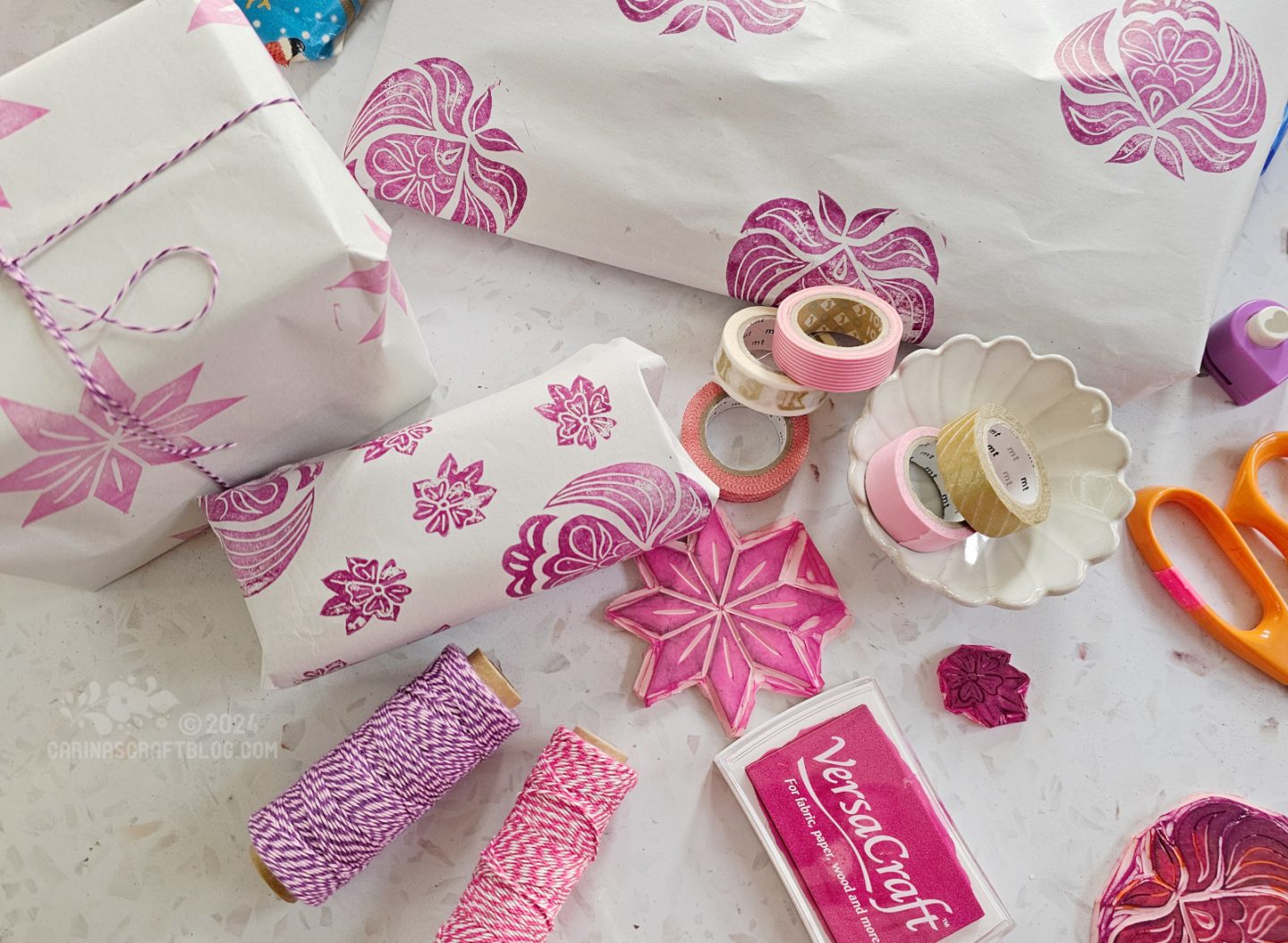 Overhead photo of a table with an assortment of wrapped presents, string in purple and pink colours, rubber stamps, and rolls of washi tape.