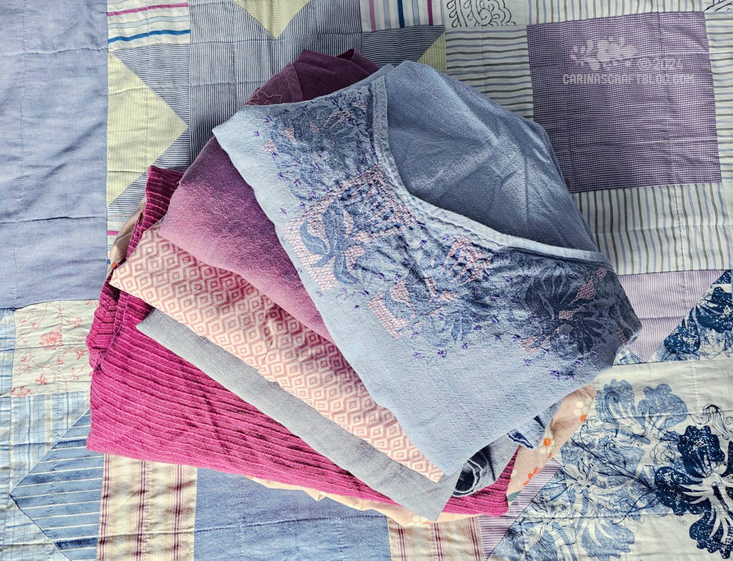 Photo of a pile of folded tops in magenta, and  dusty blue and pink colours.