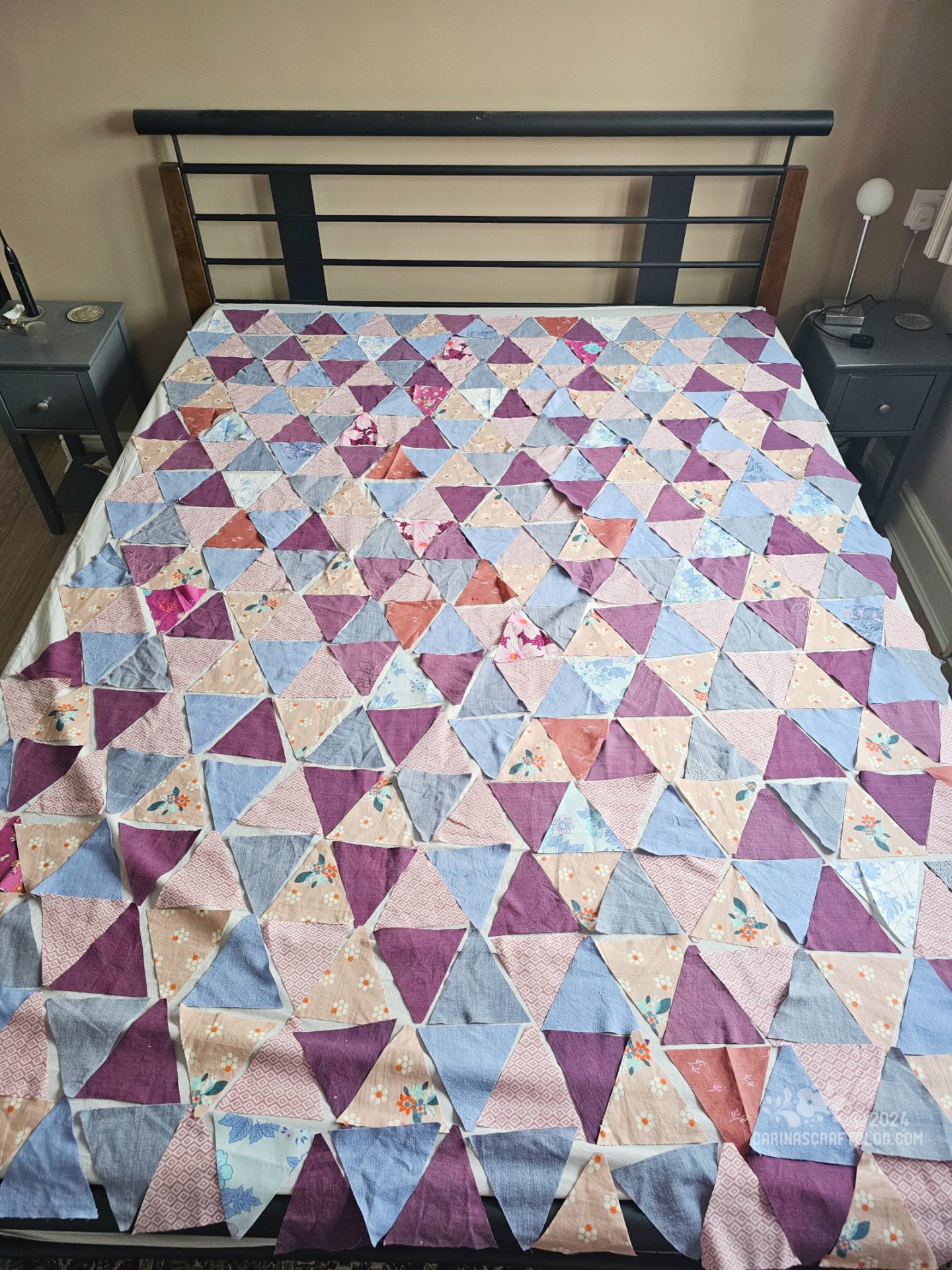 Overhead view of a bed with a quilt top laid out on it. The quilt top is made of triangles in magenta, and dusty blue and pink colours.