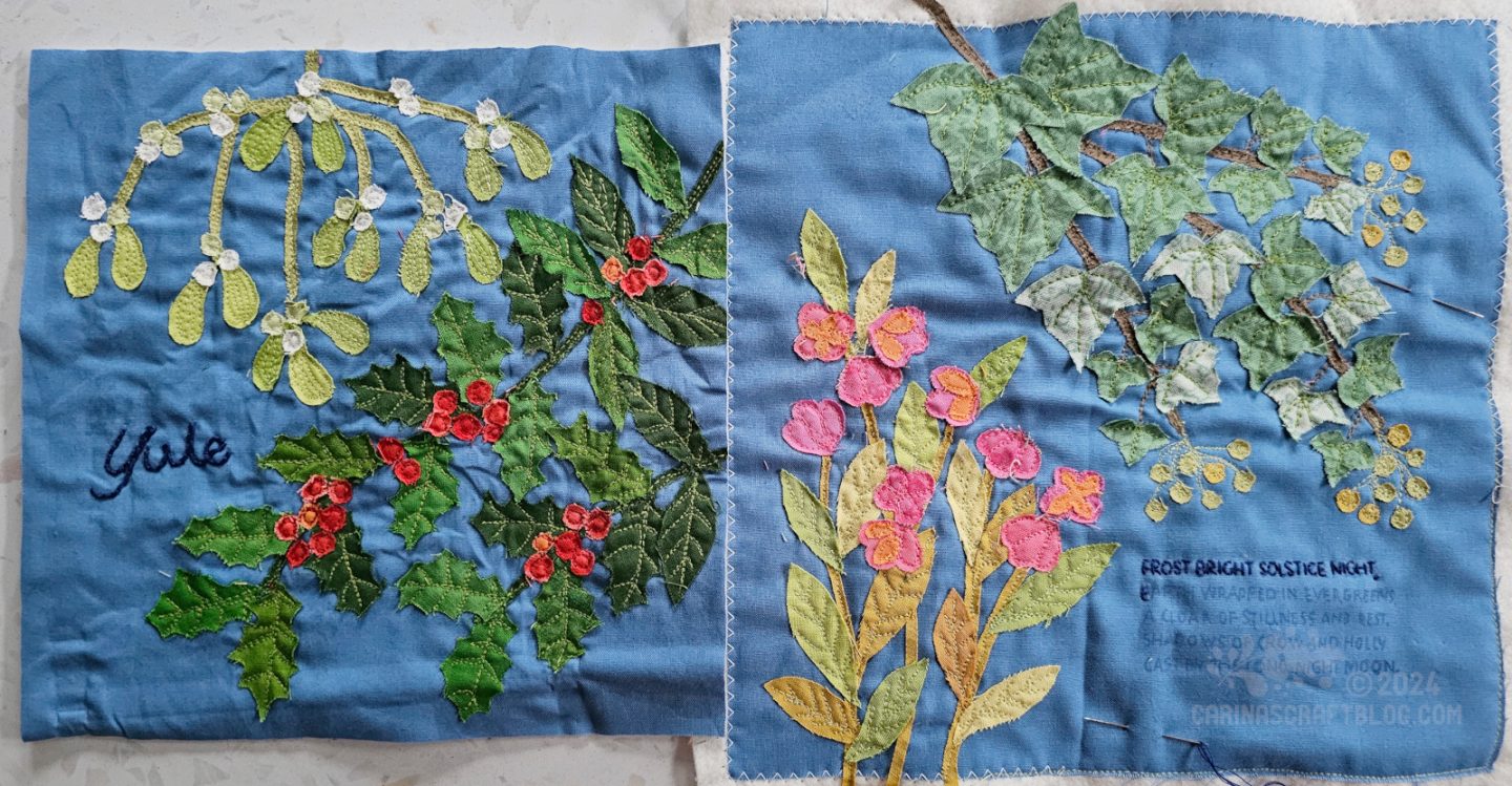 Overhead view of two medium blue fabric squares with appliqué of various plants: holly, mistletoe, ivy, and spindle.