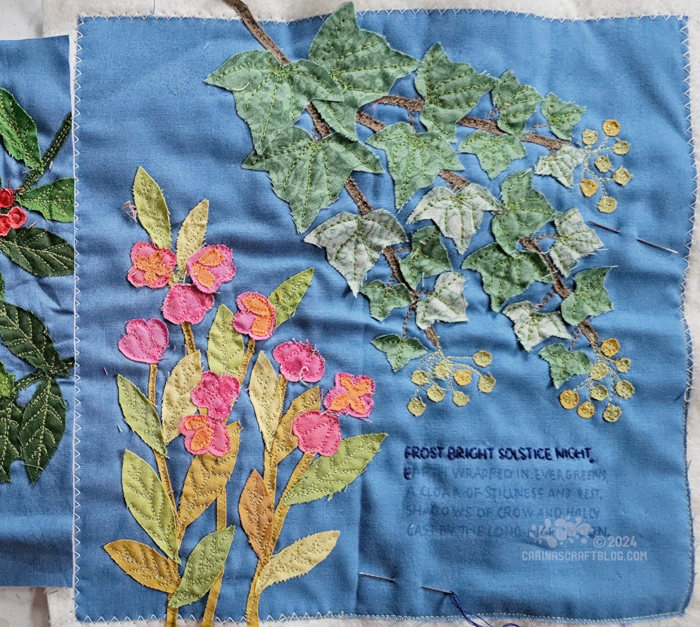 Close overhead view of a medium blue fabric square with raw edge appliqué of spindle in the bottom left half and ivy in the top right half of the photo. In the bottom right corner is a partially stitched poem.