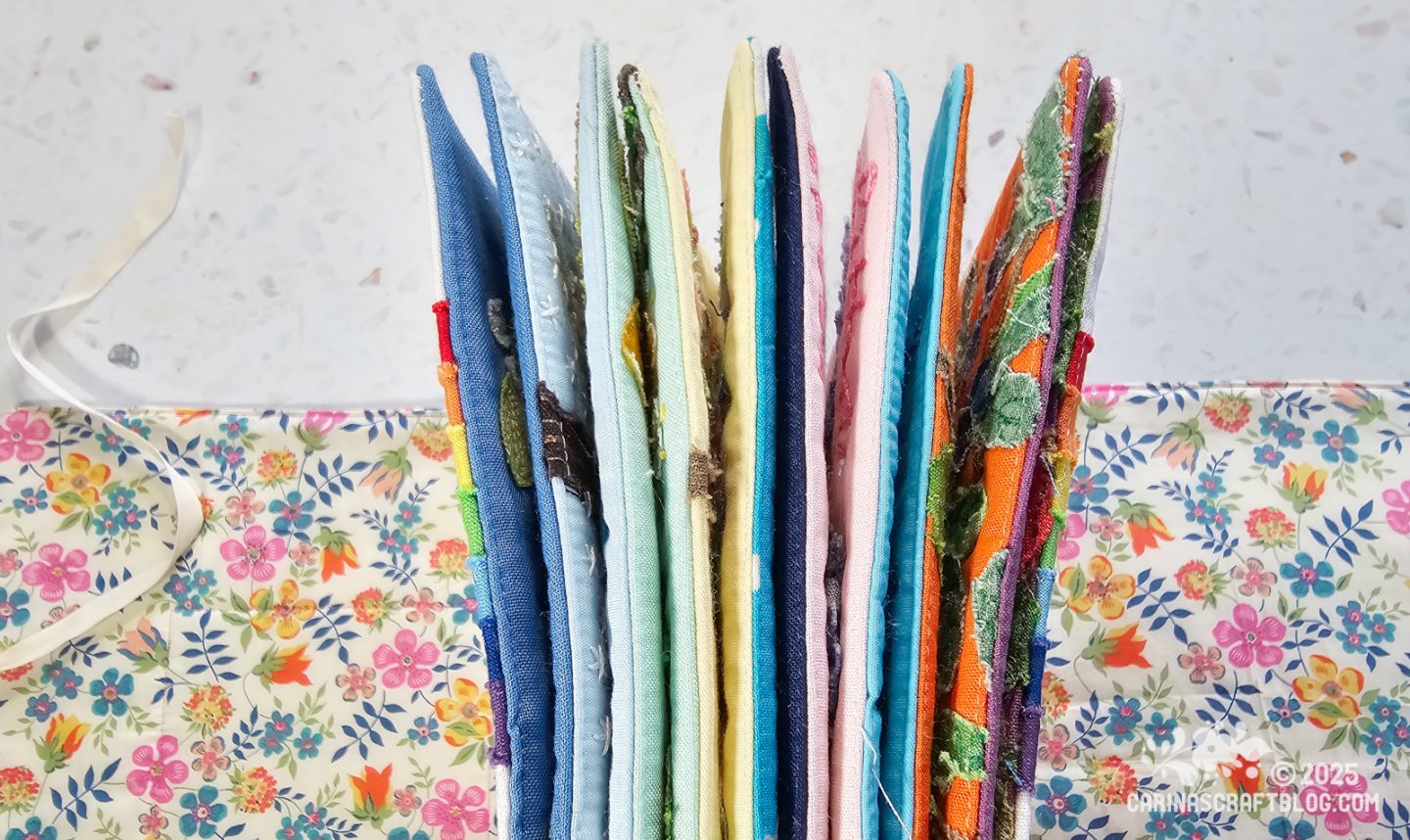 Overhead view of the edges of a textile book made of colourful pages. The open covers of the book are partially visible in the background.