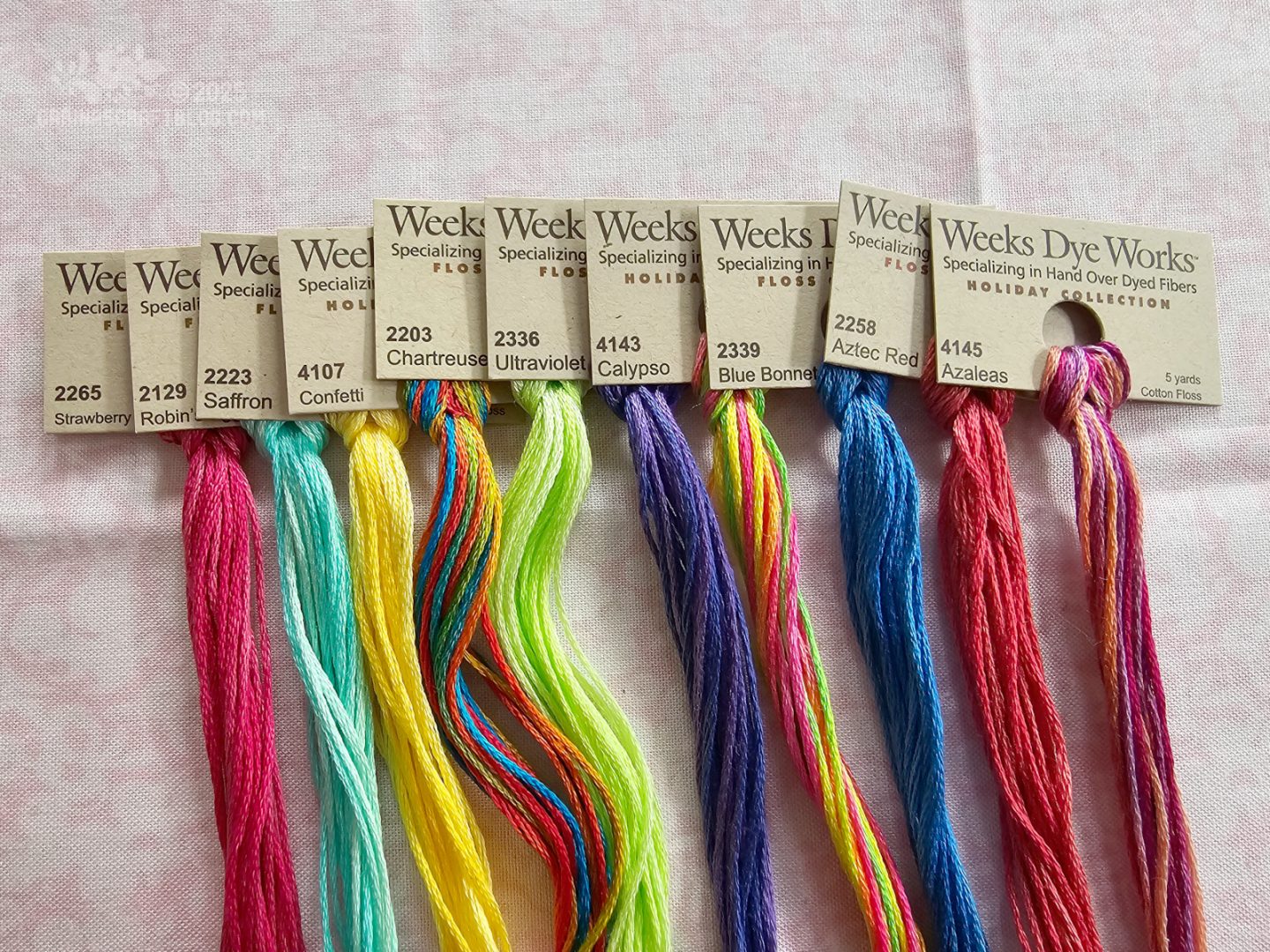 Photo. Close overhead view of colourful skeins of embroidery thread, with tags visible, displaying the company name, Weeks Dye Works, and the names of the colour.