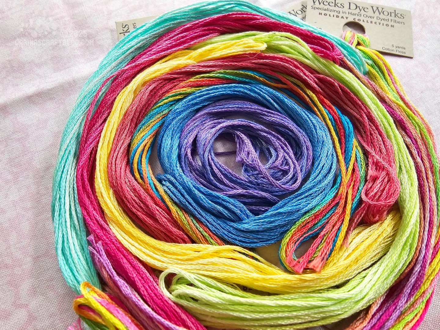 Photo. Overhead view of skeins of colourful embroidery thread laid out in a spiral of colour.