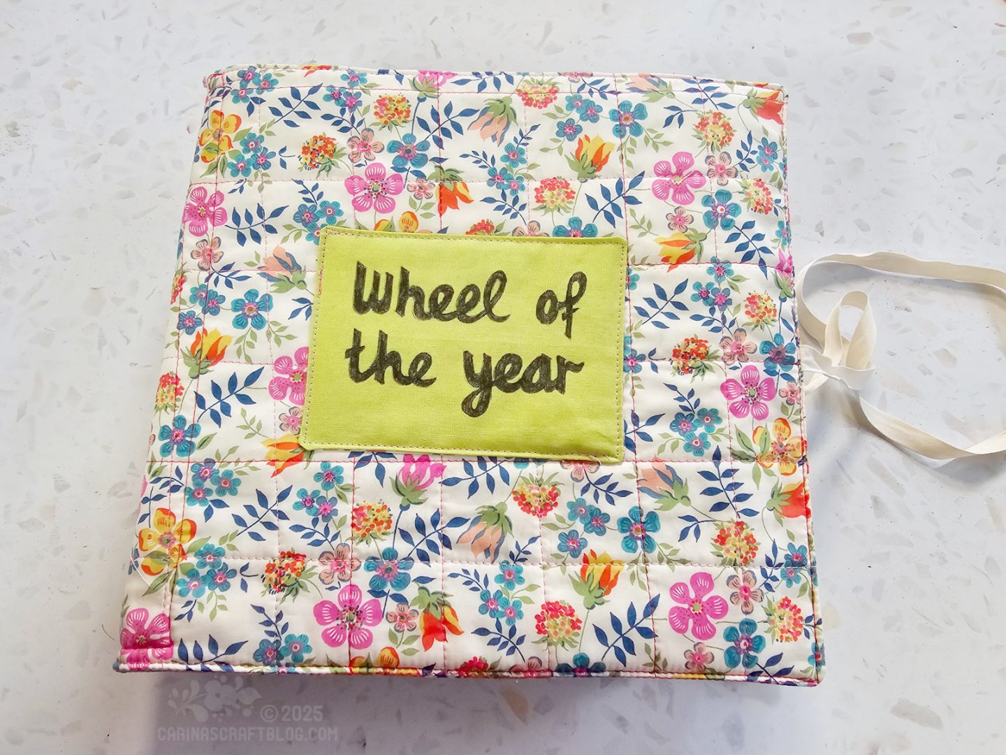 Overhead view of a fabric book with a all over floral cover and a green label with the text: Wheel of The Year.