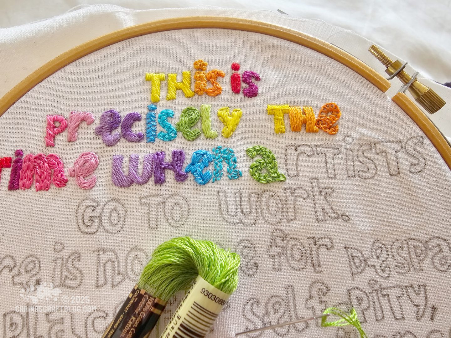 Partial view of an embroidery hoop with white fabric. A quote is traced on the fabric and some of the words have been filled in with colourful embroidery stitches.