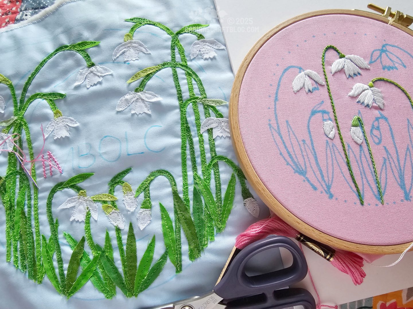 Photo. On the left of the image is a light blue square of fabric with snowdrops appliquéd on it. On the right hand side of the image is an embroidery hoop with pink fabric partially embroidered with a snowdrop design.